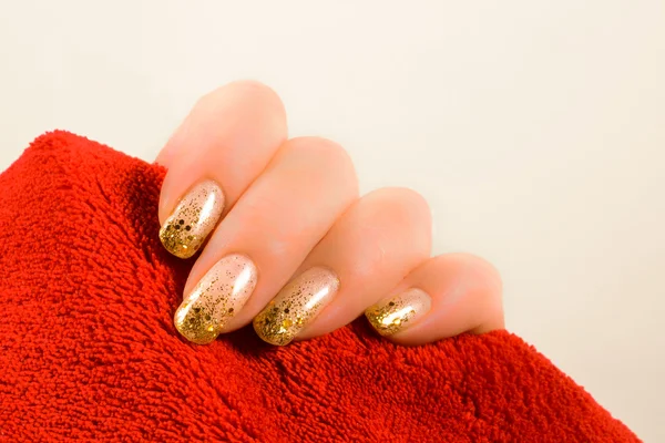 Mão com unhas de ouro segurando uma toalha vermelha — Fotografia de Stock