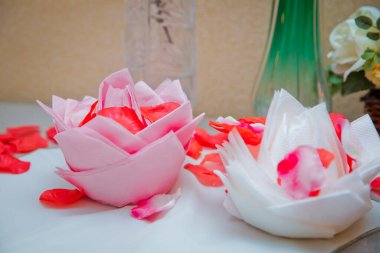 Beyaz arka planda peçeteden yapılmış güzel bir origami çiçeği. Kırmızı bir gülün yaprakları. Peçetelerin üzerinde beyaz ve pembe çiçekler.