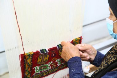 Gala 'dan geleneksel halıyı renkli yün ören kadın. Halı dokumacı onun ağzına bir maske takar. Yakın plan el yapımı halı dokuma ve üretimi. Kadın eli halı dokuyor