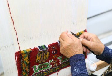 Gala 'dan geleneksel halıyı renkli yün ören kadın. Halı dokumacı onun ağzına bir maske takar. Yakın plan el yapımı halı dokuma ve üretimi. Kadın eli halı dokuyor