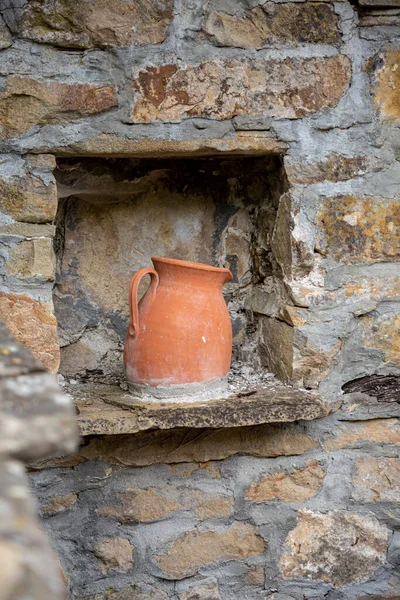 Antigua jarra de vino de arcilla hecha a mano con tela de araña de pie en una ventana de piedra en medio de la pared de piedra. decoración y artesanía para el fondo. —  Fotos de Stock