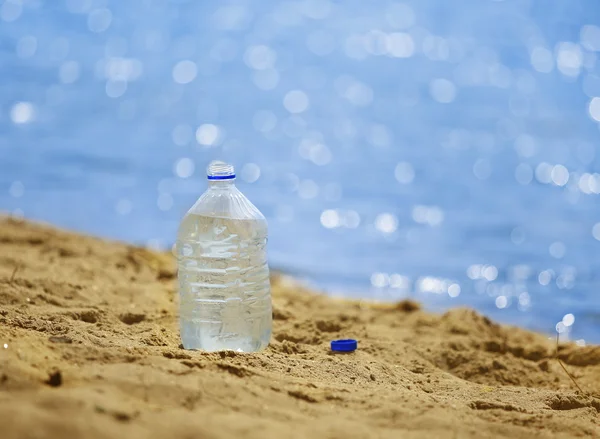 Flaska med vatten på sandiga kust — Stockfoto
