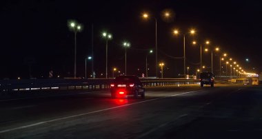 Gece yarısı banliyö otobanında sokak lambalarıyla aydınlatılmış arabalar.