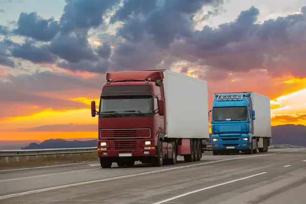 Vrachtwagens Bewegen Langs Snelweg Bij Zonsondergang Onder Een Bewolkte Hemel — Stockfoto