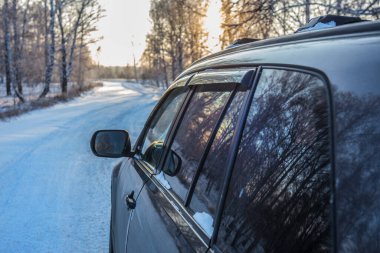 Araba gün batımında ormanda bir kış yolunda ilerliyor.
