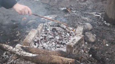 İnsan, doğada et kızartmak için sıcak kömürleri çubukla ayarlar.