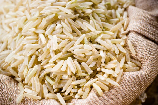 Grão de arroz orgânico cru de grão longo no saco de serapilheira - foc seletivo — Fotografia de Stock