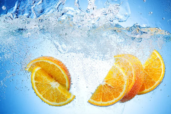 Orangenscheiben fallen mit einem großen Spritzer tief unter Wasser — Stockfoto