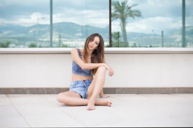 Camın yanında oturan ve kameraya bakan gündelik kıyafetli genç bir kadın.