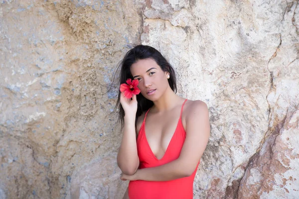 一个身穿红色泳衣的年轻女子站在岩石墙旁边看着摄像机的侧影 — 图库照片