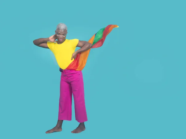 Full body positive black man with LGBT flag fluttering on waist touching neck and looking at camera against turquoise background