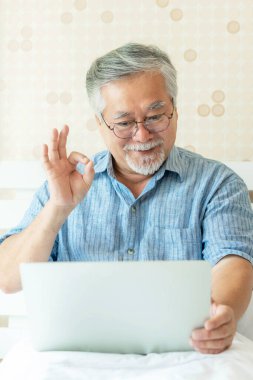 Dizüstü bilgisayar kullanan kıdemli bir Asyalı akrabalarına torun torunu olarak sesleniyor ve işaret dilini elleriyle gösteriyor, evde mutlu bir şekilde gülümsüyor - son sınıf yaşam tarzı konsepti