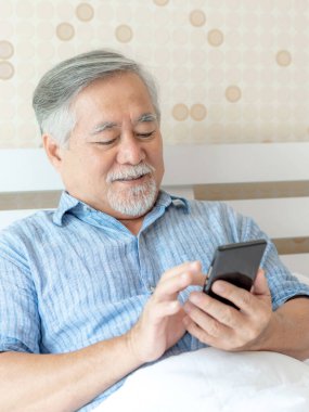 Akıllı telefon kullanan yaşlı bir erkek, gülümseyerek evde mutlu ol - yaşam tarzı son sınıf konsepti