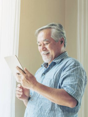 Akıllı telefon kullanan yaşlı bir erkek, gülümsüyor. Yatak odasında mutlu hissediyor. Son sınıf yaşam tarzı konsepti.