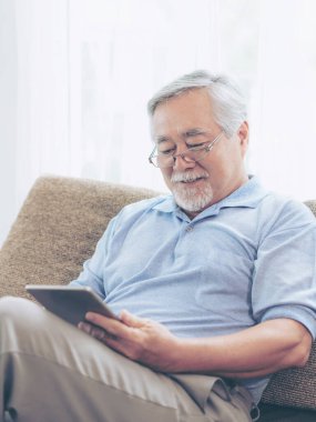 Akıllı telefon kullanan, gülümseyen, evdeki koltukta mutlu hisseden son sınıf öğrencisi. Yaşlılar konsepti.