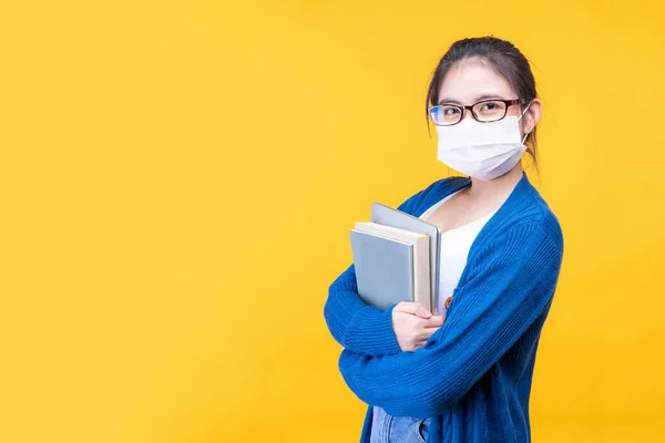 Portrait of a beautiful young woman student wear a mask holding textbook  - studying online e-learning system during the corona virus covid19 outbreak