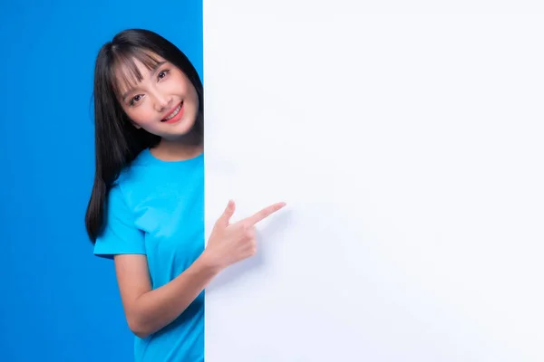 美しいアジアの若い女性とともに前髪のあるスタイルで青Tシャツ笑顔と指差す指広告バナーのための空白のスペース 空のスペースホワイトボード青の背景に隔離された空白のバナー — ストック写真