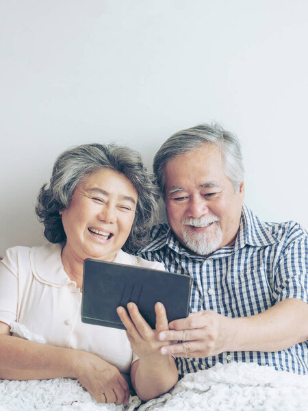 Senior couple using a tablet phone computer face time call to relatives descendant relatives grandchild, smiling feel happy in sofa at home - lifestyle senior concept