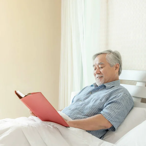 Senior Male Reading novel book , smiling feel happy on bed at home - lifestyle senior happiness concept