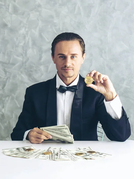 İş adamı zengini tüccar Bitcoin altın sikkesi tutuyor Bitcoin tüccarı için yeni para değişimi ve masa başı iş konsepti üzerine Amerikan doları banknotları