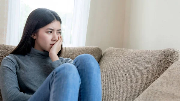 Close up face of unhappy Asian pretty young woman siting alone on couch with feeling sadness , emotional young woman was depressed on sofa