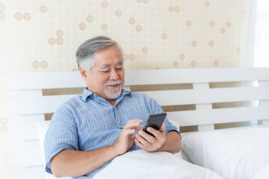 Üst düzey erkek, Asyalı yaşlı adam akıllı telefon kullanıyor evde yatakta iyi sağlık - yaşam tarzı son sınıf konsepti