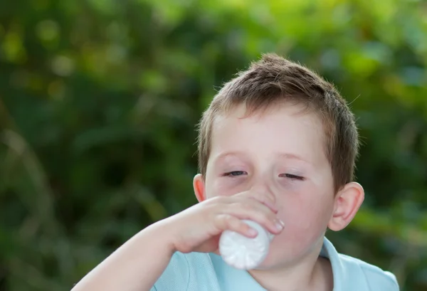 Niño bebiendo leche de una pequeña botella blanca —  Fotos de Stock