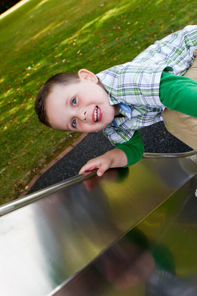 little boy sliding down a side at the park