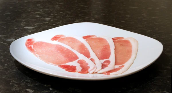 Éruptions cutanées non cuites de bacon sur une assiette blanche — Photo