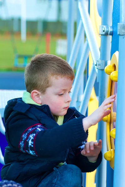 Liten pojke spelar på appratus i parken — Stockfoto