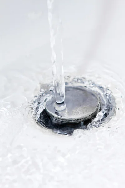 Acqua che scorre lungo un foro del lavandino del bagno — Foto Stock