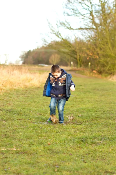 Kleine jongen spetteren in een plas op het gebied — Stockfoto