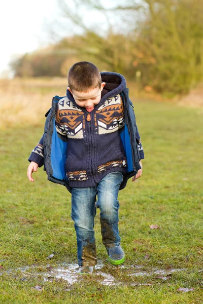 Kleine jongen spetteren in een plas op het gebied — Stockfoto