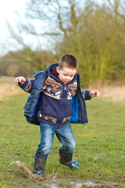 Kleine jongen spetteren in een plas op het gebied — Stockfoto