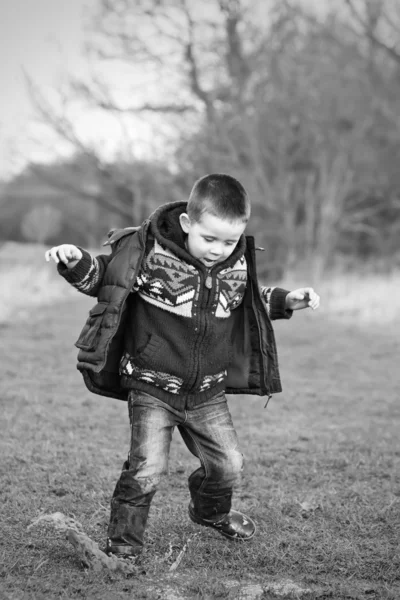 Kleine jongen spetteren in een plas op het gebied — Stockfoto