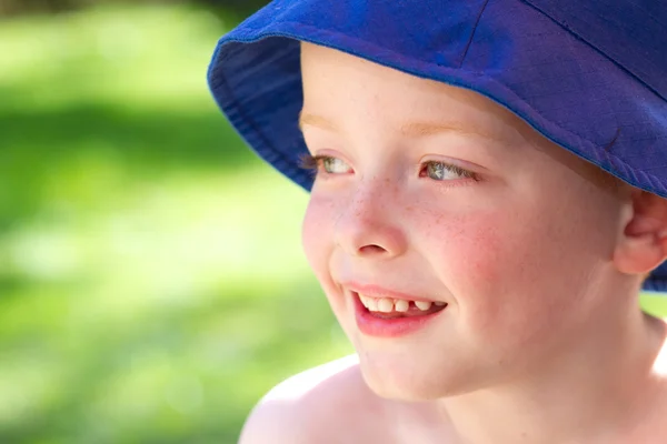 Lindo niño pequeño con un sombrero de sol en el jardín sonriendo de alegría — Foto de Stock