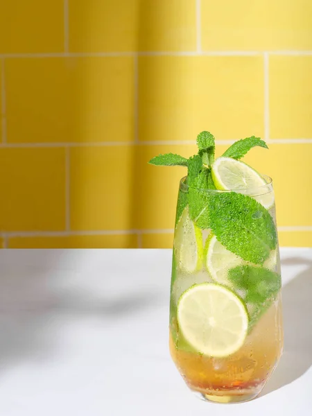 Mojito or virgin mojito long rum drink with fresh mint, lime juice, cane sugar and soda. On yellow background.