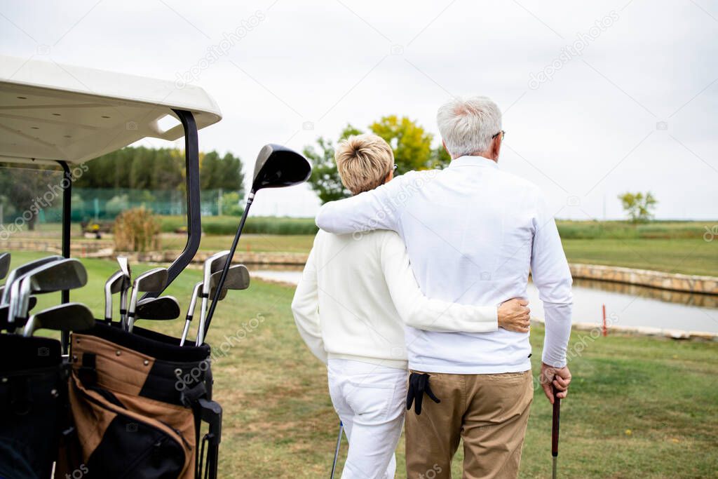 Senior couple holding together and enjoying recreational time in retirement by playing golf.