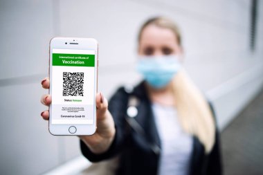 Covid-19 Corona virüsüne karşı aşı olduğunu onaylamak için telefonunda QR kodu bulunan dijital sağlık pasaportu ya da sertifikası olan genç bir kadın..