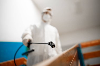 Beyaz steril koruyucu giysili bir adam Corona virüsü salgını sırasında okul sınıfındaki merdivenleri ve koridorları dezenfekte ediyor ve dezenfekte ediyor..