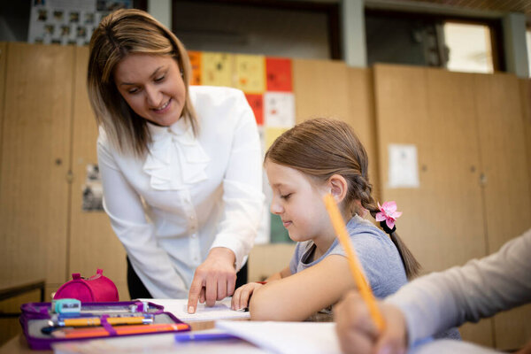 Caucasian schoolteacher helping children with their tasks in classroom.