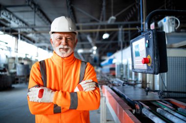 Yüksek görüşlü ceketli profesyonel fabrika işçisi veya mühendisi endüstriyel üretim salonundaki otomatik makinenin yanında duruyor. Fabrikanın içi..