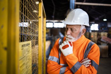Üretim fabrikasında yüksek görünür üniformalı ve sıkı şapkalı endüstriyel işçiler yeni güvenlik düzenlemeleri okuyorlar..