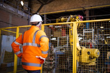 Üretim departmanında endüstriyel robot kolu kontrol eden güvenlik üniforması içindeki fabrika işçisi.