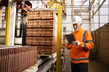 Çatı kiremit fabrikasında çalışıyor. Çalışan ambalaj makinesinin yanında duruyor ve süreci kontrol ediyor.