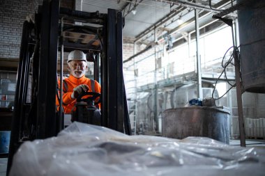 Üniformalı son sınıf beyaz erkek ve fabrika deposunda forklift kullanan beyaz kasklı..