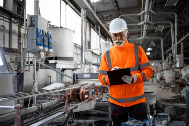 Endüstriyel işçi danışmanı makine başında ve imalat fabrikasındaki üretimi kontrol ediyor..