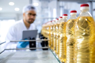 Bottled vegetable oil production in food factory and worker in white coat with hairnet controlling process. clipart