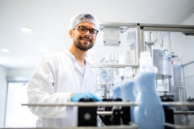 Kimya fabrikasında duran teknoloji uzmanının portresi ve yerli kullanım için deterjan, sıvı sabun ve kumaş yumuşatıcıları üretimini kontrol etmek.