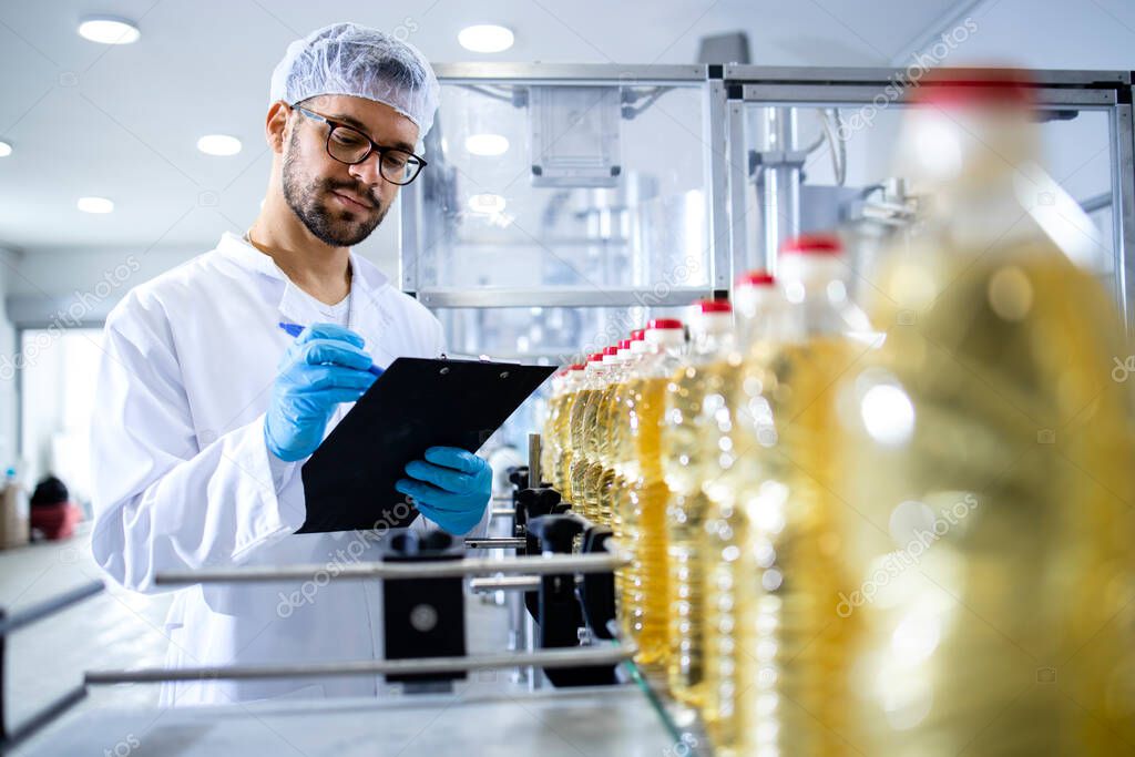 Food factory worker taking notes and controlling production line of edible oil.